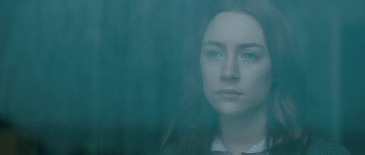 Byzantium (2012) movie still: closeup — The face of a young woman is seen partially obscured by a glass surface. She remains still with a neutral…