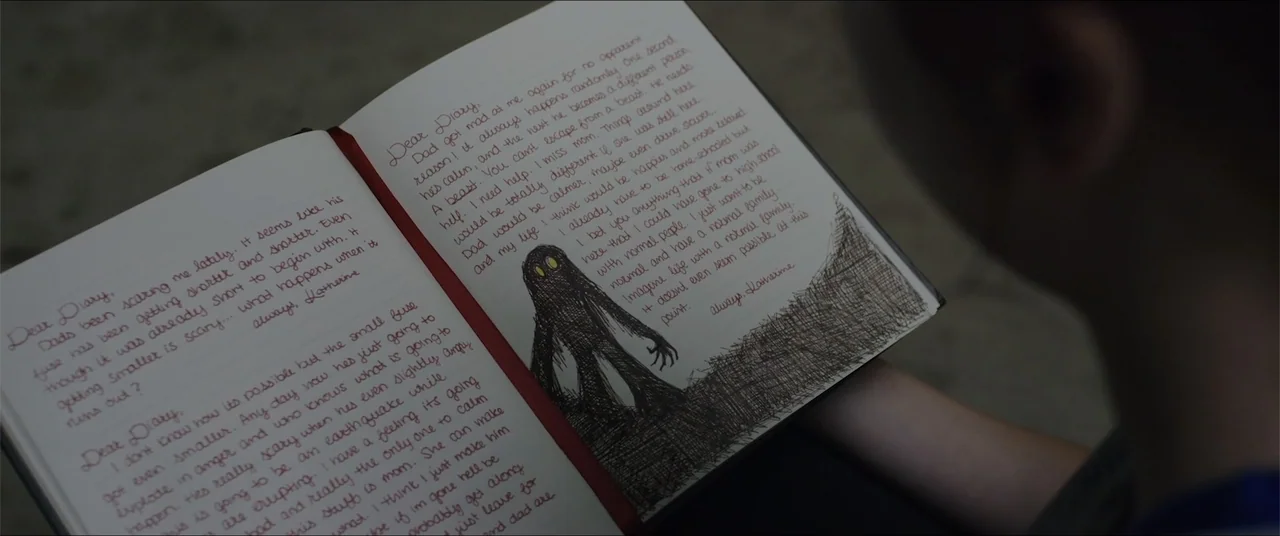 Captive (2020) movie still: closeup — A personal diary lies open with handwritten text and a dark creature drawing. A person holds the journal and…