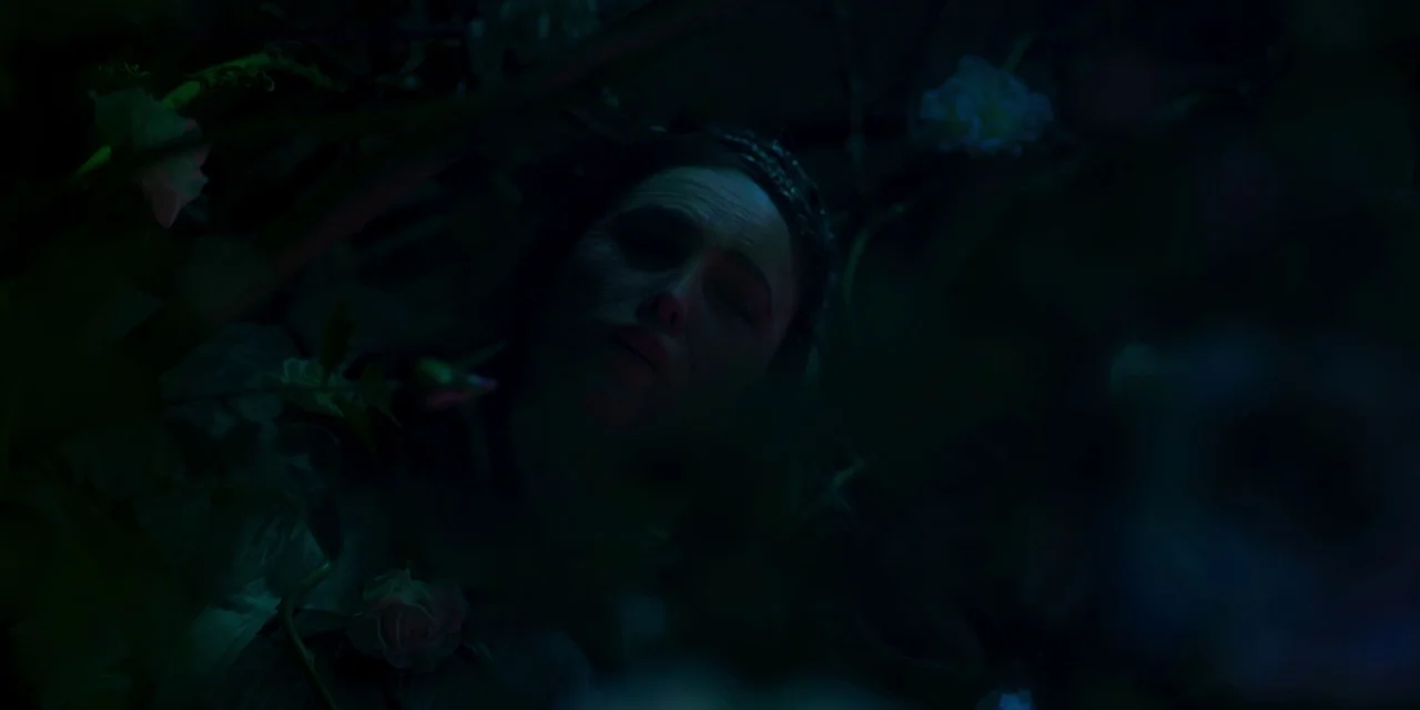 Paradise Hills (2019) movie still: closeup — A woman rests among dense dark foliage and pale flowers at night. Her face is illuminated by faint blue…