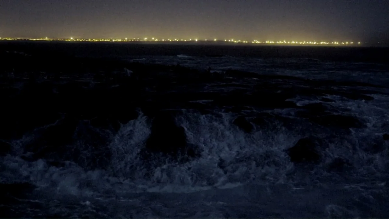 Air Jaws: Night Stalker (2016) movie still: establishing — A rocky shoreline at night is battered by dark, foamy ocean waves. A distant horizon…