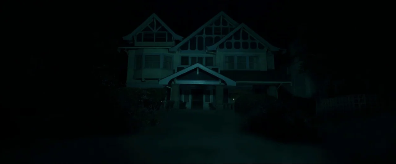 Insidious (2010) movie still: establishing — A two-story residential house with timber framing stands silhouetted against a dark night sky. The…
