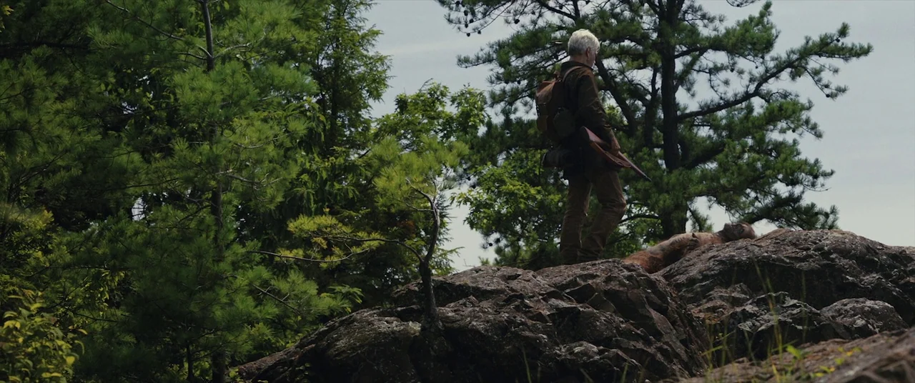 The Man Who Killed Hitler and Then the Bigfoot (2018) movie still: wide — A high, rocky outcrop is surrounded by dense pine trees under an overcast…
