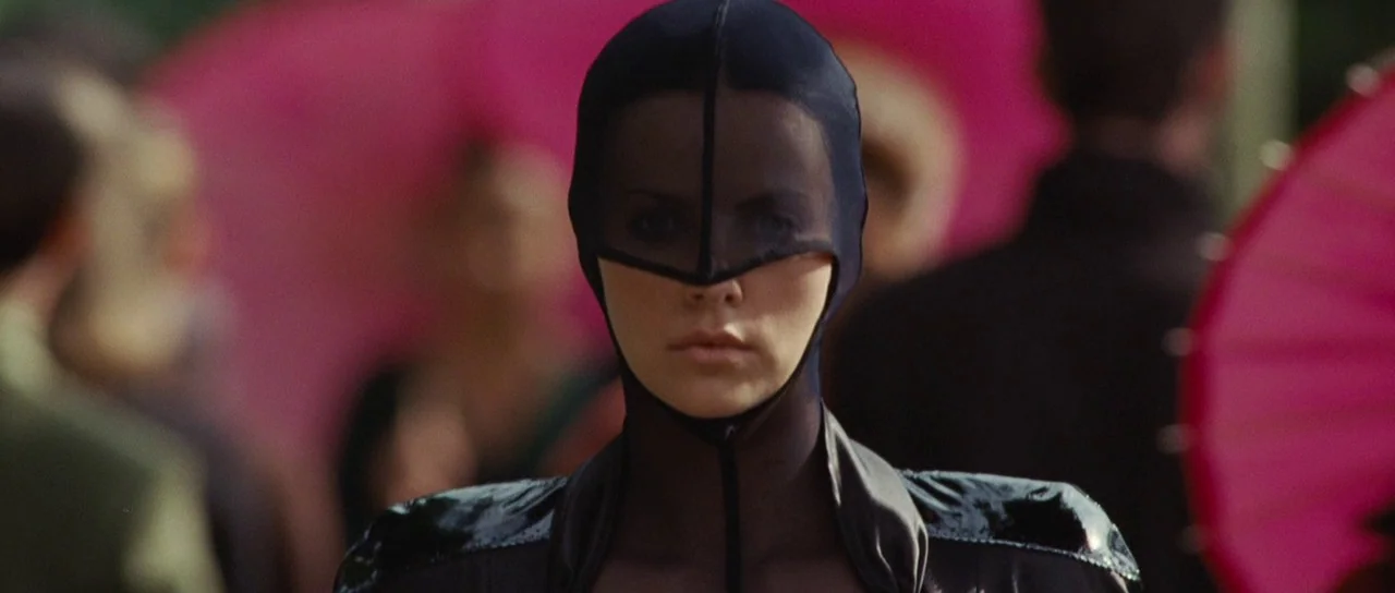 Aeon Flux (2005) movie still: closeup — A crowded public event features people holding pink umbrellas under diffused daylight. A woman wearing a…