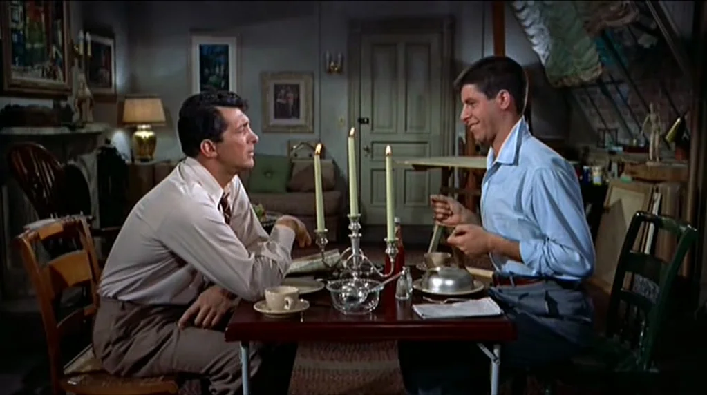Artists and Models (1955) movie still: medium — A furnished interior space featuring a dark wood dining table and modest home decor. Two men sit…