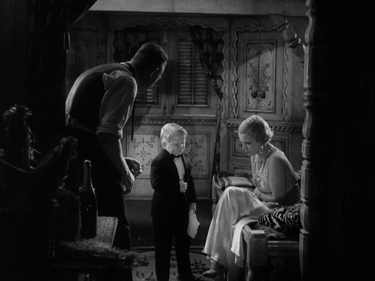 Freaks (1932) movie still: medium — A dark, wood-paneled room with detailed carved doors and decorative accents. Three people stand in a triangular…