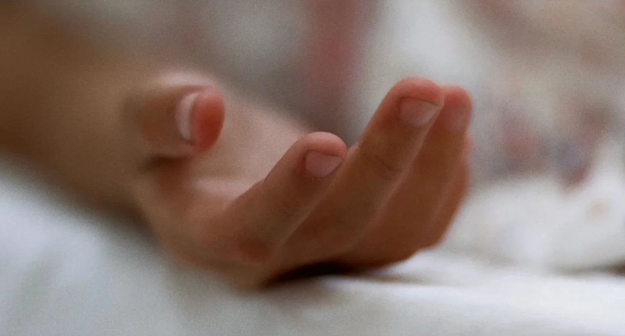 The Killer (1989) movie still: closeup — A close-up of an open human hand resting against a soft white fabric surface. The fingers are slightly…