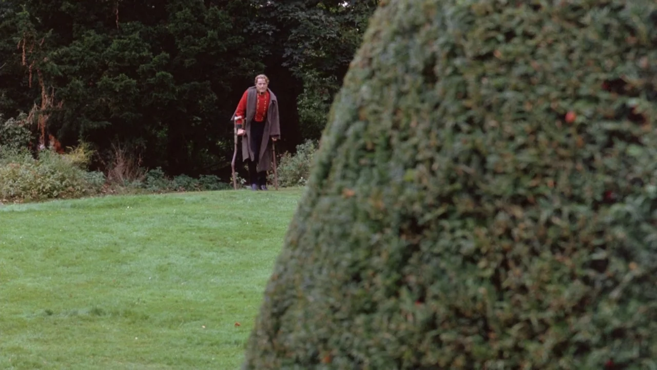Mountains of the Moon (1990) movie still: wide — A man stands on a green lawn with tall dark trees in the background. The man uses two wooden…