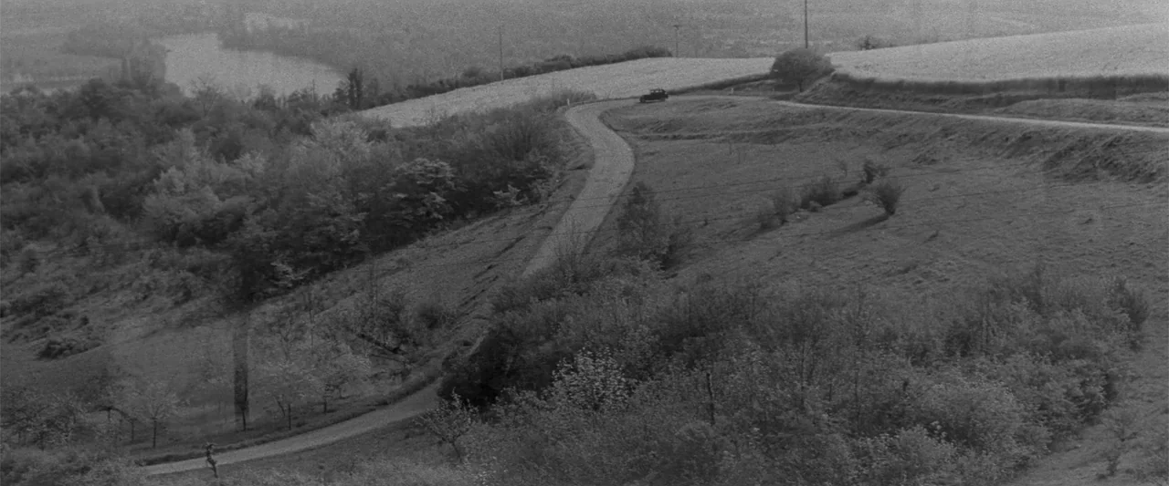 Jules and Jim (1962) movie still: wide — A rural landscape features a winding narrow road cutting through hills and dense greenery. A single small…