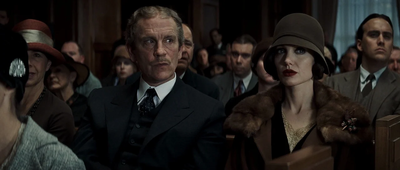 Changeling (2008) movie still: medium — A crowded wooden courtroom gallery filled with people wearing early twentieth-century formal attire. A man…