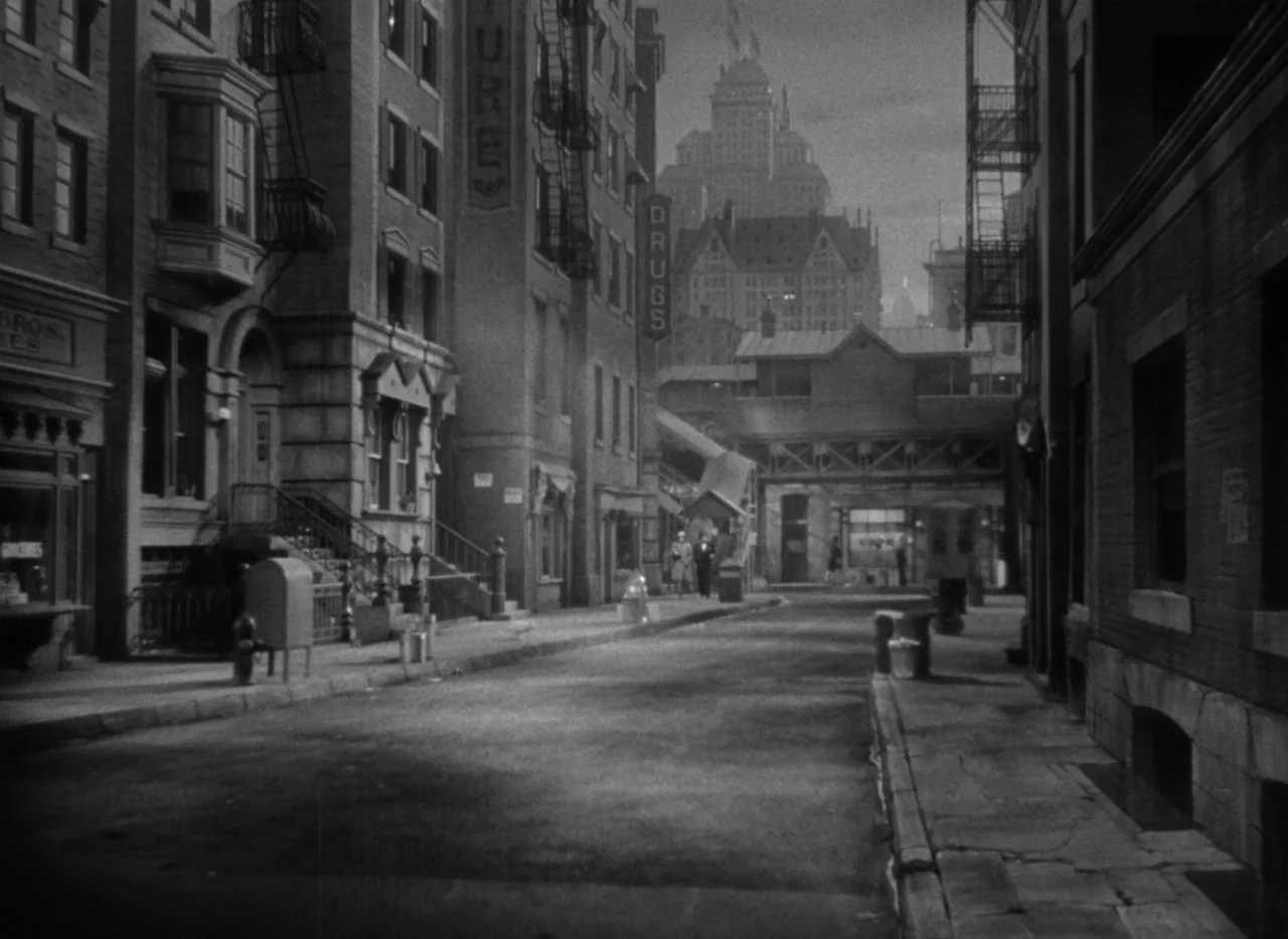 Dance, Girl, Dance (1940) movie still: establishing — An urban street scene features brick buildings with fire escapes and vertical neon signs. A…