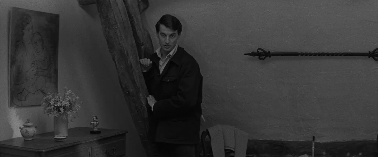 Jules and Jim (1962) movie still: medium — A rustic attic interior features plastered walls and a large vertical wooden support timber. A young man…