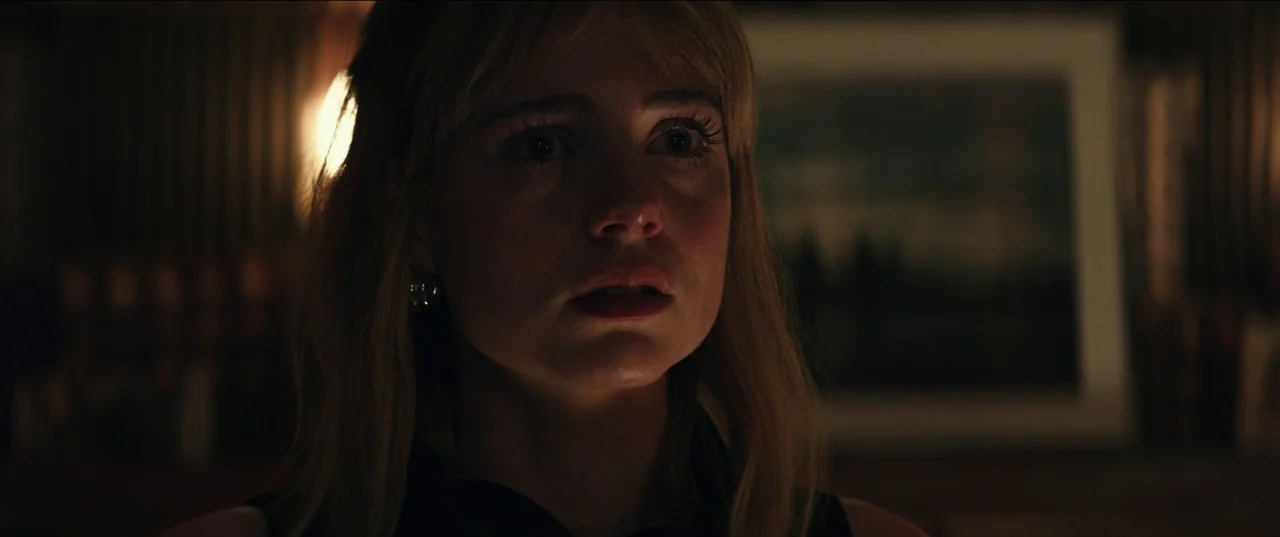 The Greatest Hits (2024) movie still: closeup — A dimly lit room provides a dark, indistinct backdrop for a human face. A woman with blonde hair…