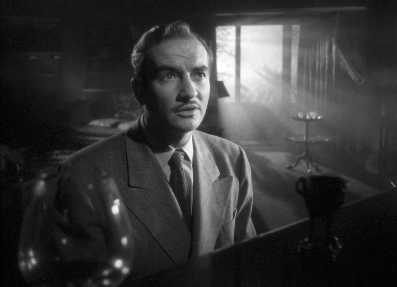 The Amazing Mr. X (1948) movie still: medium — A dimly lit room with a window featuring light beams filtering through haze. A man in a suit looks…