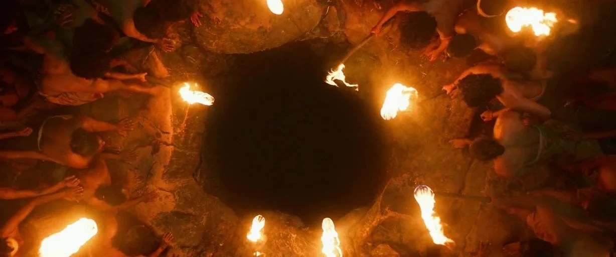 Kantara: A Legend - Chapter 1 (2025) movie still: wide — A group of people stands in a circle around a dark central pit. Each person holds a bright…