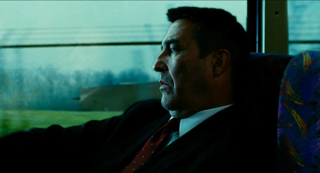 Life During Wartime (2009) movie still: medium — A man in a suit rides a bus past a blurred landscape. He sits near the window while observing the…