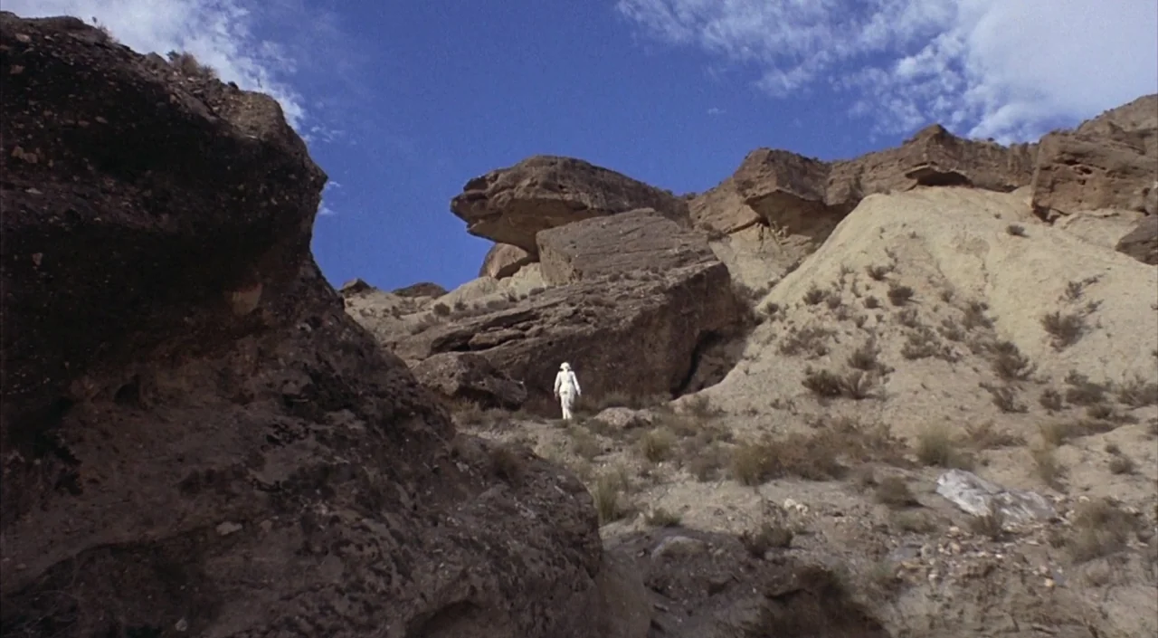 Dr. Phibes Rises Again (1972) movie still: wide — A vast, arid desert landscape features layered rock formations and sparse desert vegetation. A…