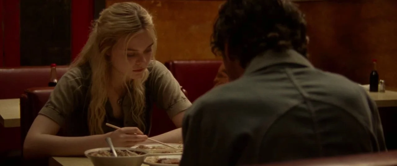 Low Down (2014) movie still: medium — A diner booth with red vinyl seating and warm, textured walls provides a setting. A blonde woman and a man in…