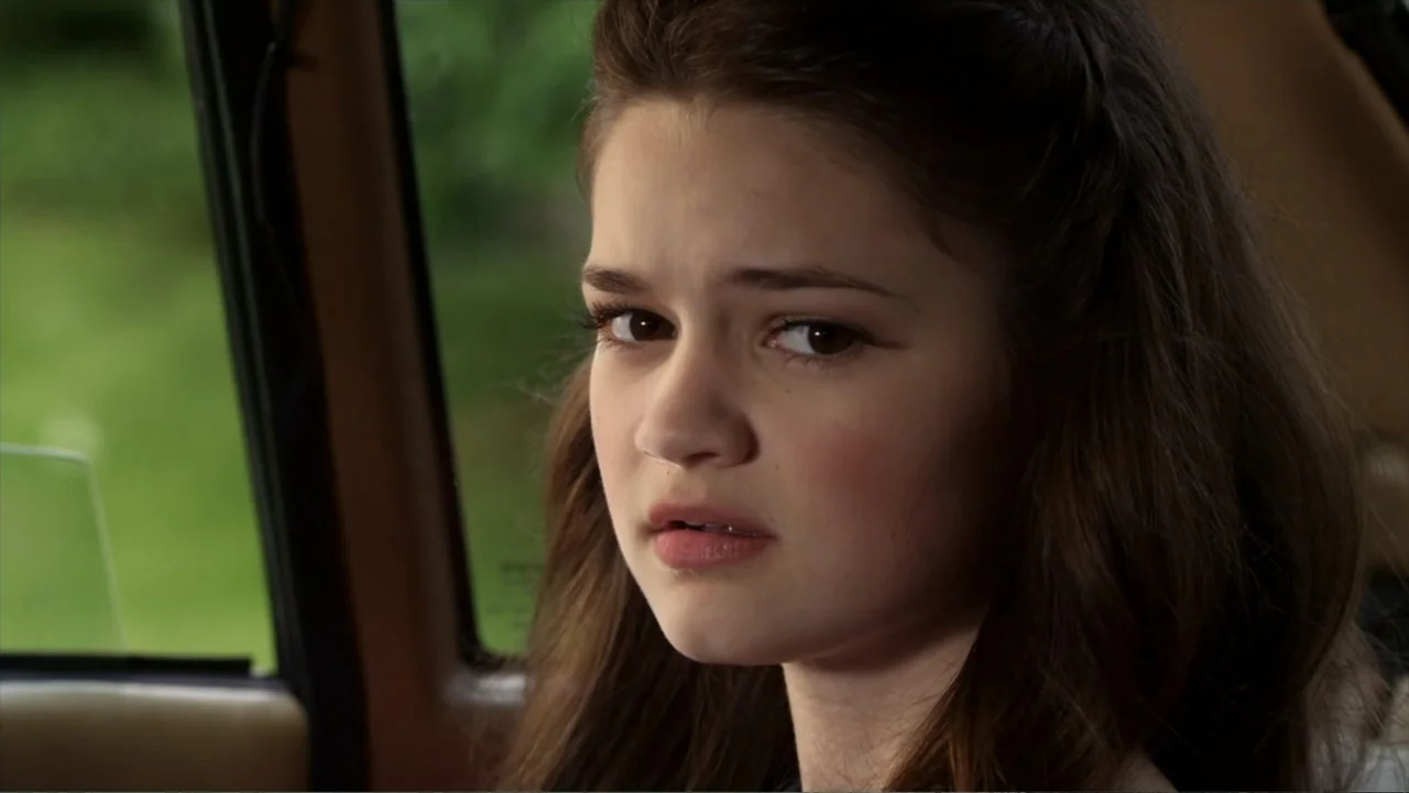 Jinxed (2013) movie still: closeup — The interior of a car during the day with green foliage visible outside. A teenage girl sits in the passenger…