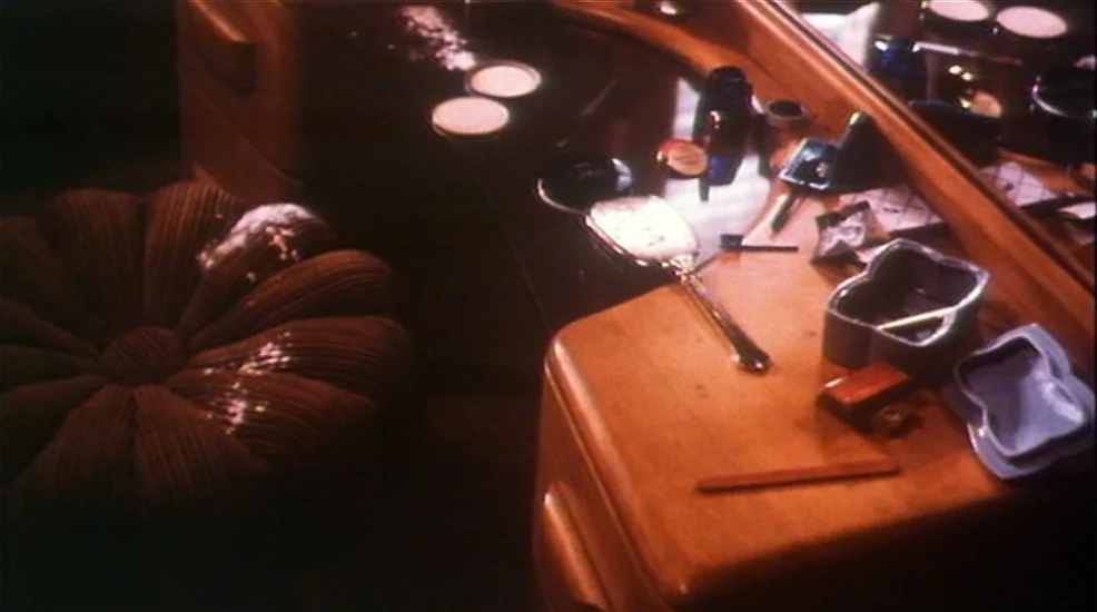 Union City (1980) movie still: medium — A wooden vanity top holds scattered makeup containers and a hand mirror. A plush brown floral-patterned…