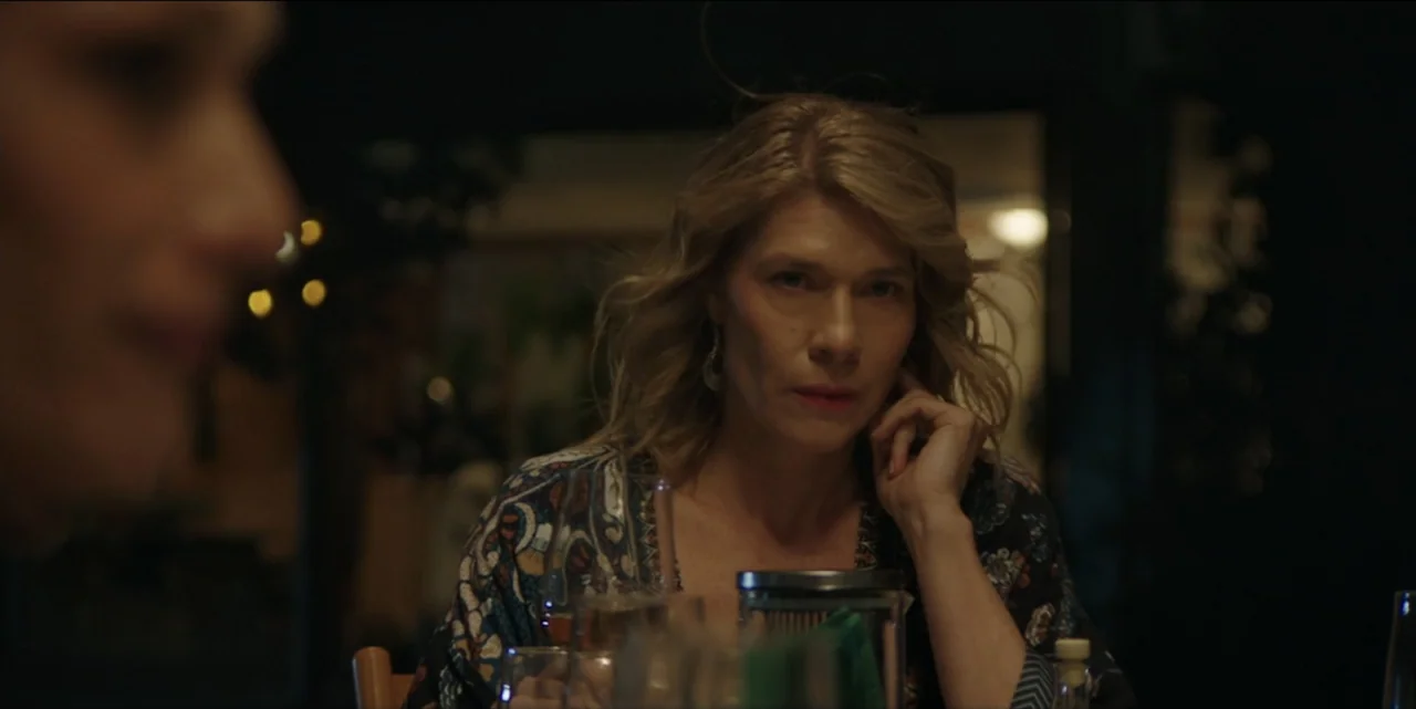 The Hunted (2024) movie still: medium — A dimly lit restaurant interior features blurred foreground and background elements. A woman sits at a table…