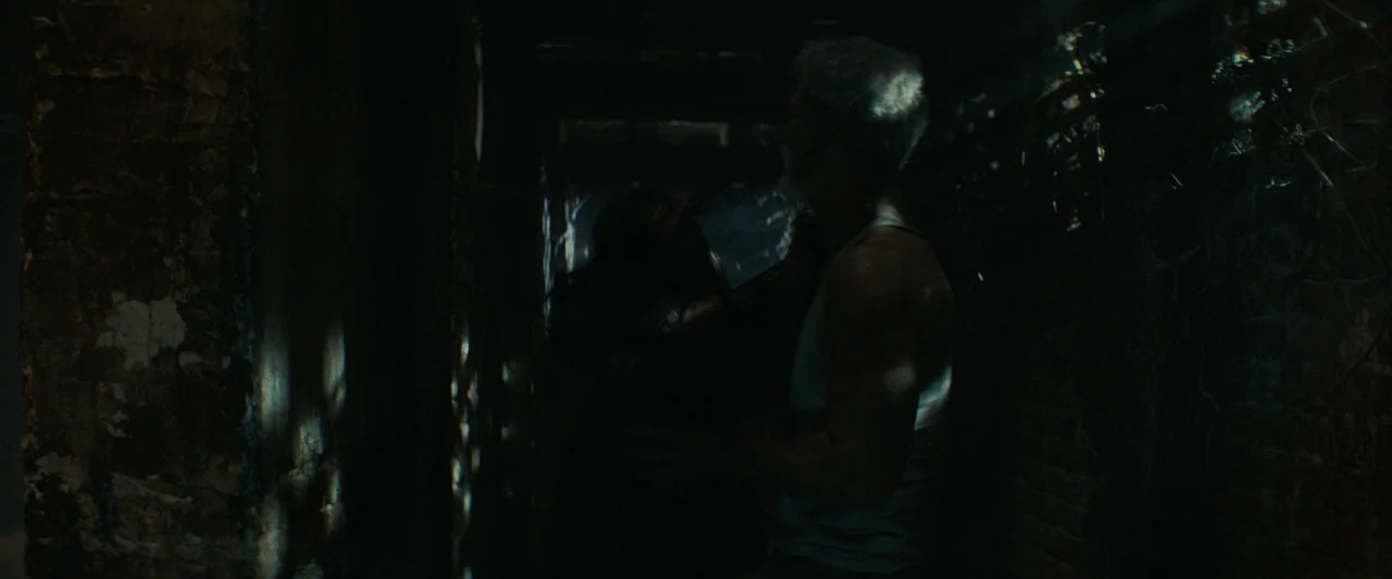 Don’t Breathe 2 (2021) movie still: medium — A dark, narrow corridor with textured walls features dim lighting. An older man stands close to a…