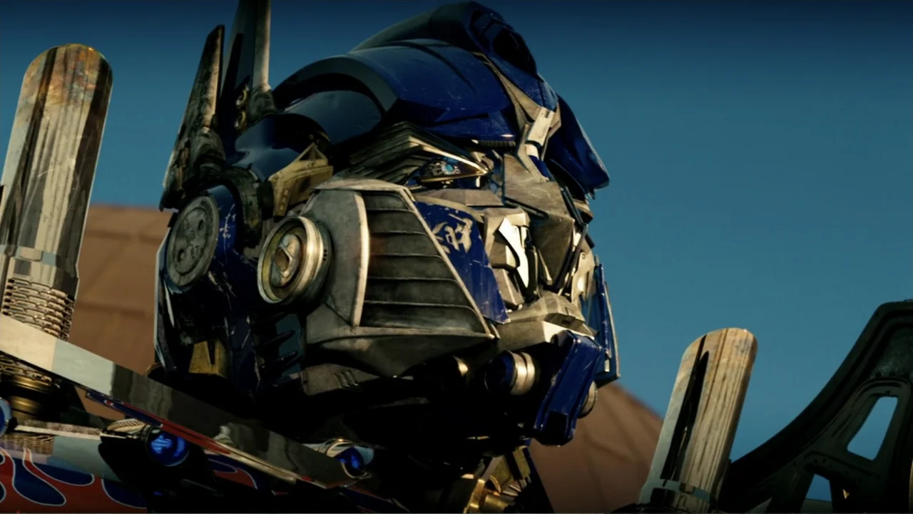 Transformers (2007) movie still: closeup — A giant metallic robot head stands against a clear blue desert sky background. The robot exhibits…