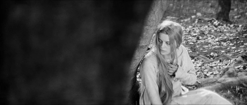 Marketa Lazarová (1967) movie still: medium — A woman leans against a thick tree trunk in a dense, leaf-covered woodland. She holds her hand to her…