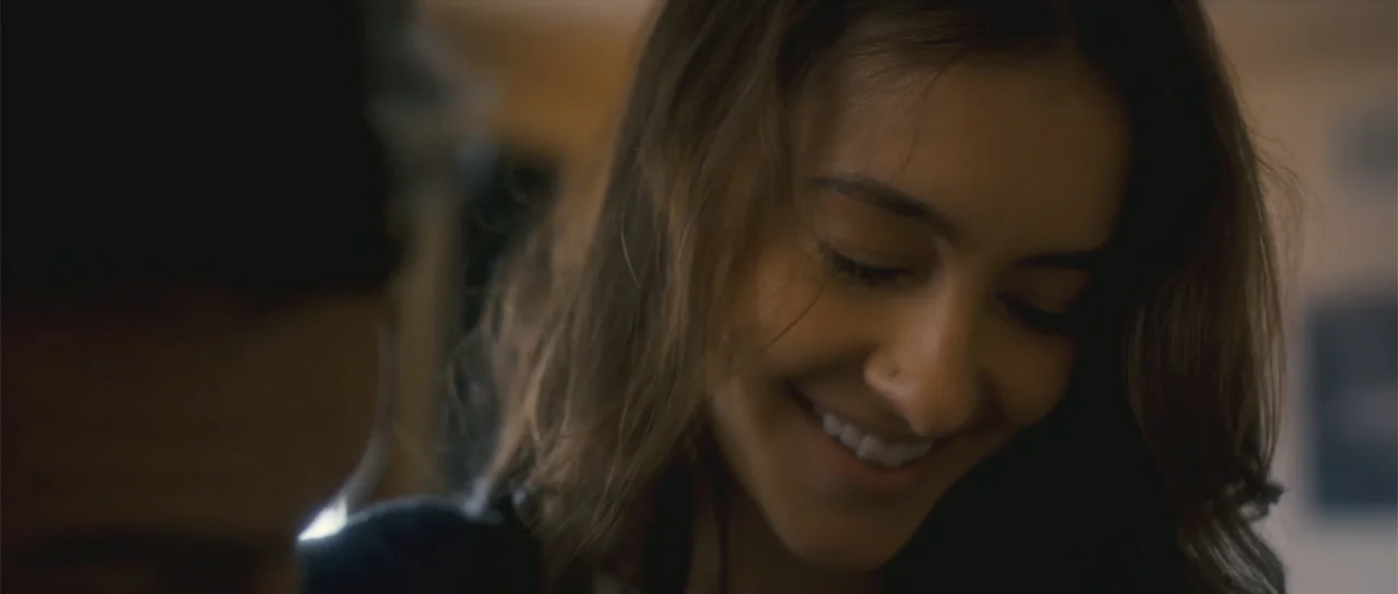 Night of the Missing (2023) movie still: closeup — An indoor living space with a blurred out-of-focus background area. A young woman looks down and…