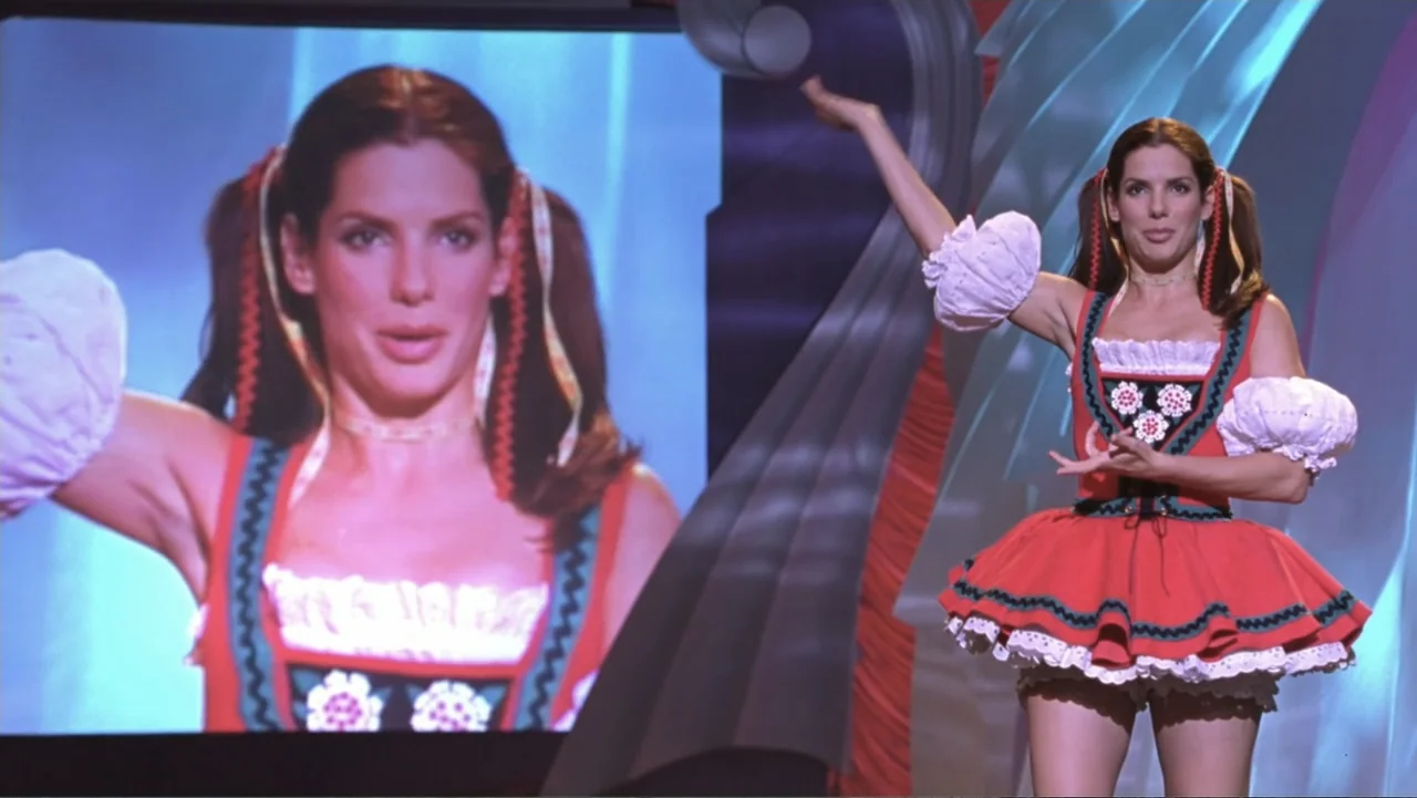 Miss Congeniality (2000) movie still: medium — A television studio set featuring a brightly colored backdrop and a large projection screen. A woman…