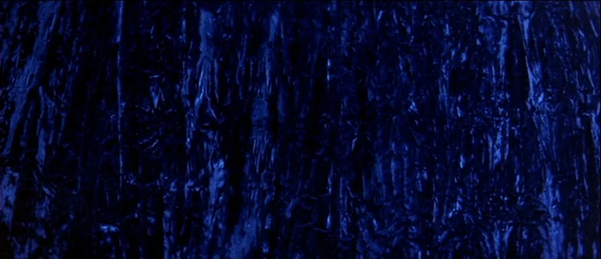 Blue Velvet (1986) movie still: closeup — A close-up view of the vertical, rough ridges and deep crevices of tree bark. Dark blue lighting…