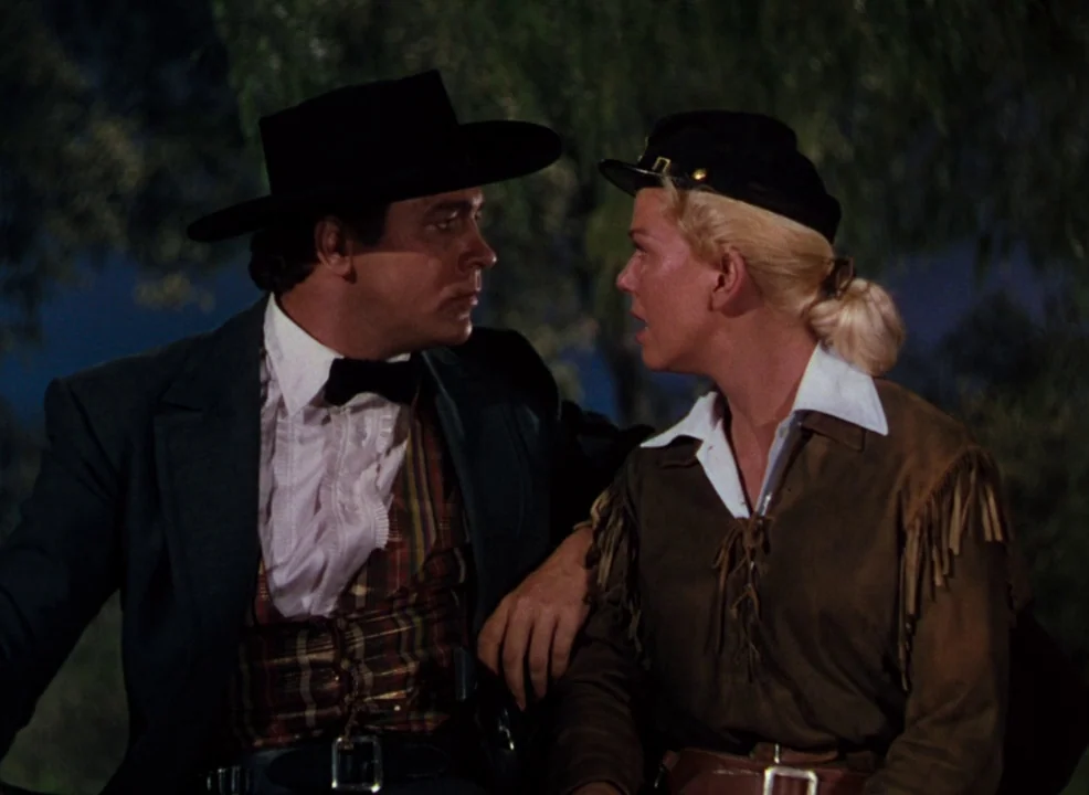 Calamity Jane (1953) movie still: medium — Two individuals in western clothing sit outdoors under the dark night sky. They are positioned closely…