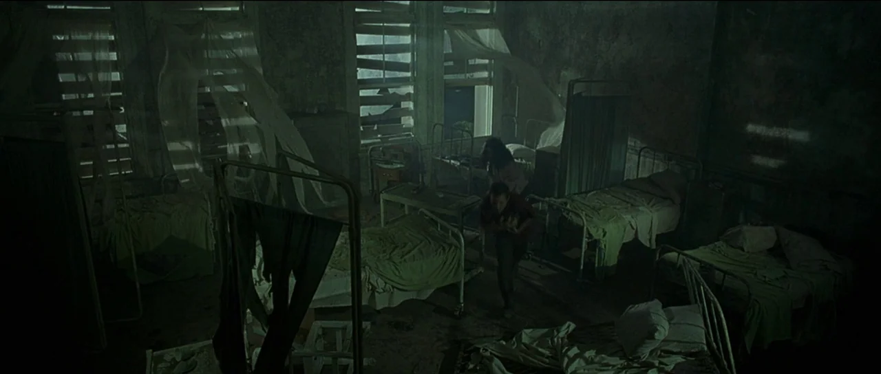 The Frighteners (1996) movie still: wide — A dark, dilapidated medical ward features multiple iron beds with torn, aged linens. A man and a woman…