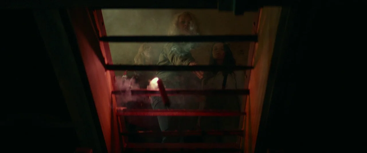 Halloween (2018) (2018) movie still: medium — Three women stand at the top of a dark staircase in a smoke-filled room. They look down as a single…