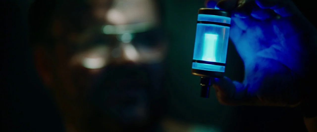 Child's Play (2019) movie still: closeup — A dark space lit primarily by a singular, bright blue glowing object held by hand. A man with goggles…