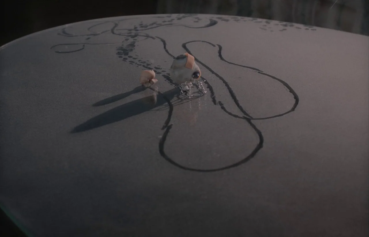 Marcel the Shell with Shoes On (2021) movie still: closeup — A dust-covered surface features hand-drawn lines resembling a path or map. Small…