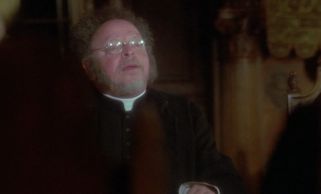 The Strange Case of Dr. Jekyll and Miss Osbourne (1981) movie still: medium — A man in clerical attire stands in a room with dark wood paneling. He…