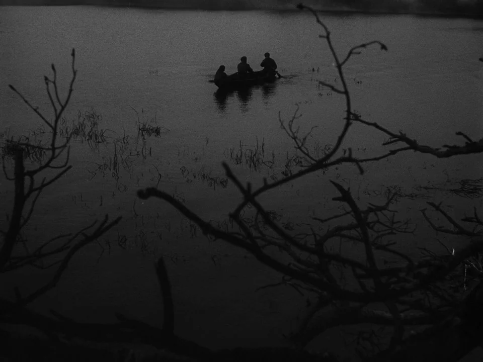 Ivan’s Childhood (1962) movie still: wide — A dark body of water is framed by foreground branches of leafless trees. Three silhouetted figures…
