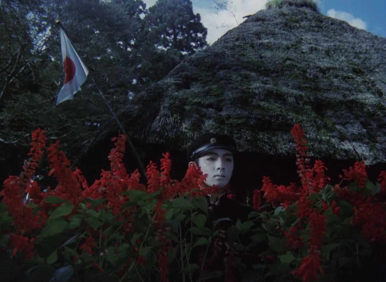 Pastoral To Die In The Country (1974) movie still: medium — A traditional Japanese farmhouse with a thatched roof sits behind a field of red…