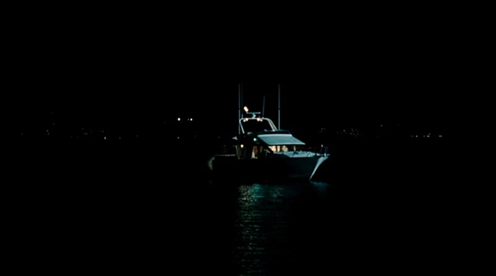 Visioneers (2008) movie still: wide — A motorboat floats on the surface of calm black water in the middle of night. The vessel emits a dim warm glow…
