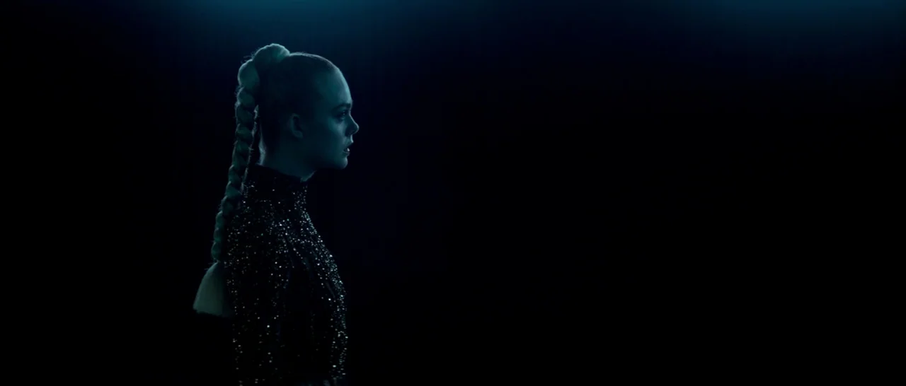 The Neon Demon (2016) movie still: medium — A woman stands in a featureless black environment with no visible architectural structures. She is lit…