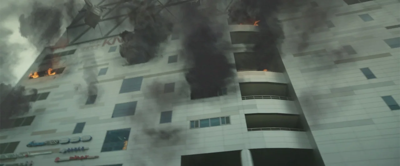Along with the Gods: The Two Worlds (2017) movie still: establishing — A large multi-story commercial building exterior is engulfed in thick black…