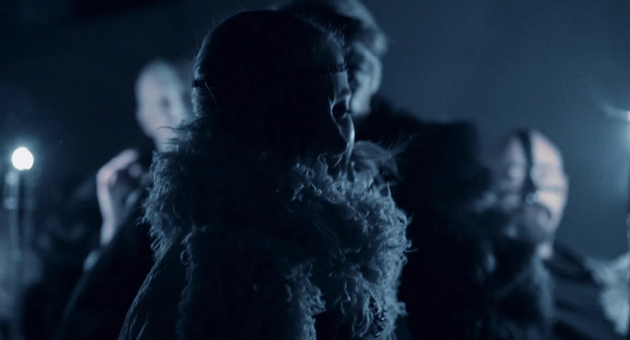 All You Need Is Death (2023) movie still: medium — A dimly lit room filled with shadows and unidentified figures standing in the dark. A woman in a…
