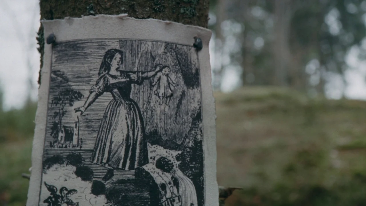 The Devil’s Bath (2024) movie still: closeup — A detailed monochromatic print is tacked onto the textured bark of a forest tree. The illustration…