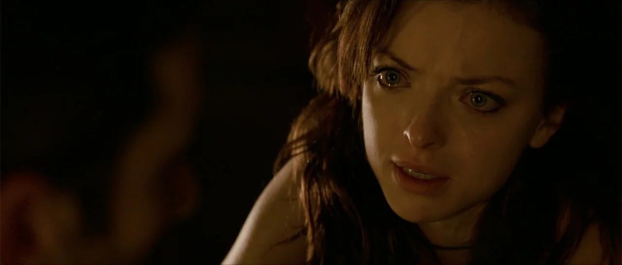 The Vault (2017) movie still: closeup — A dark indoor setting with minimal detail visible in the low light. A young woman with long brown hair looks…