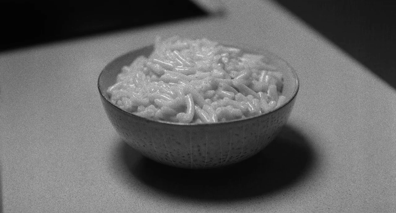 Malcolm & Marie (2021) movie still: closeup — A ceramic bowl filled with macaroni and cheese rests on a flat gray surface. The bowl has a textured,…