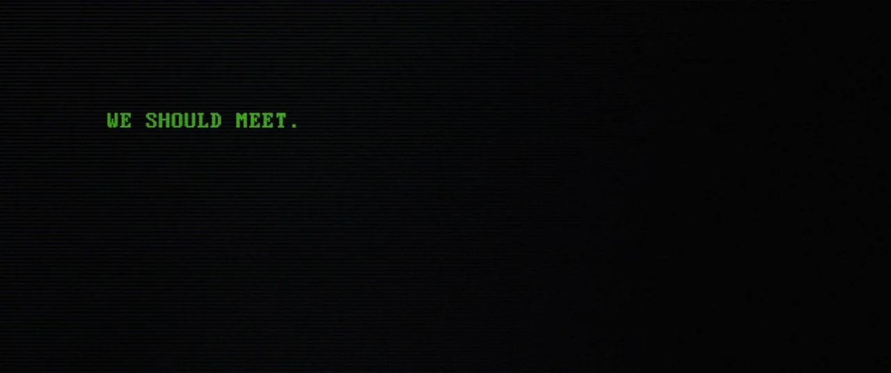 Broadcast Signal Intrusion (2021) movie still: establishing — A dark computer screen displays a single line of bright green digital text. The text…