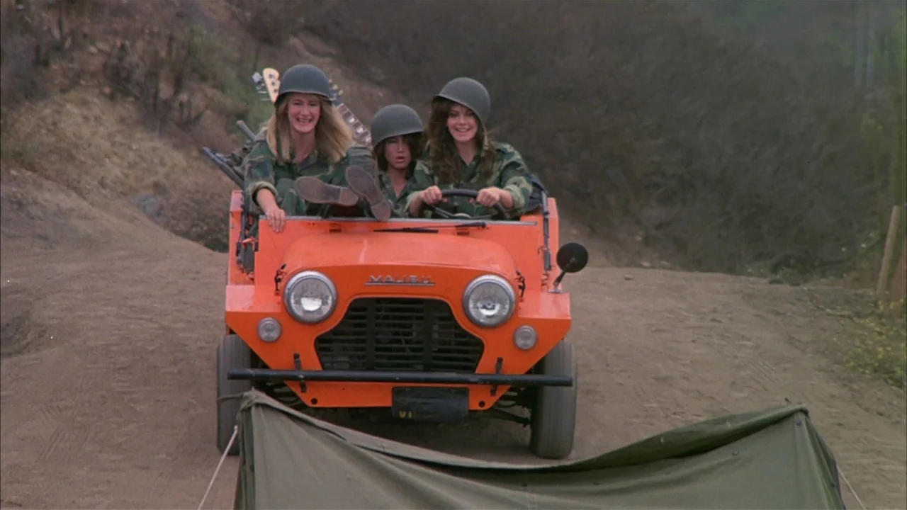 Ladies and Gentlemen, the Fabulous Stains (1985) movie still: fullbody — A bright orange vintage jeep drives along a dusty, uneven dirt path…