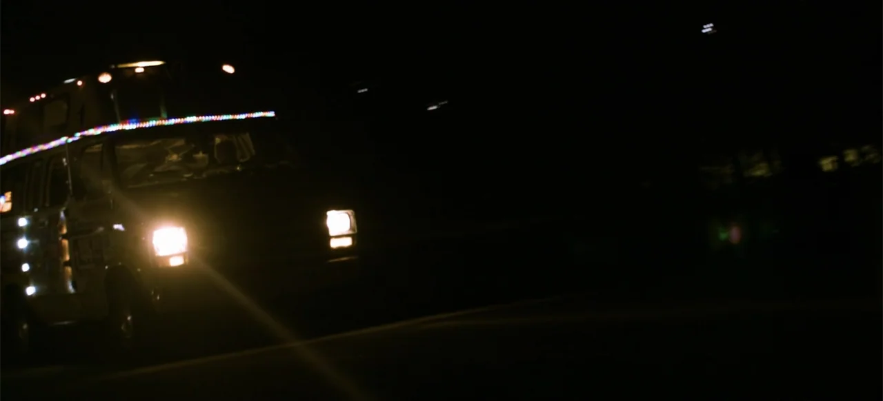 Hellbreeder (2004) movie still: wide — A dark road at night with the headlights of a van approaching. The van is decorated with thin strings of…