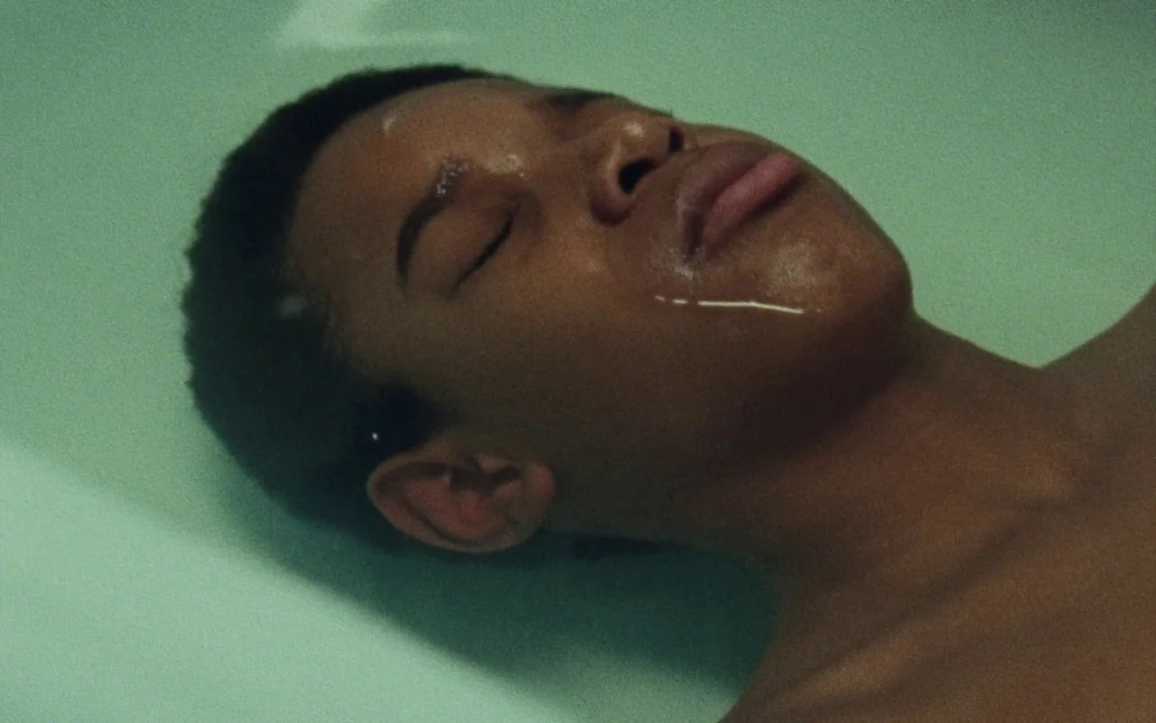 Education (2020) movie still: closeup — A close-up view shows a person submerged to their chin in a bathtub. Water rests along the jawline while the…