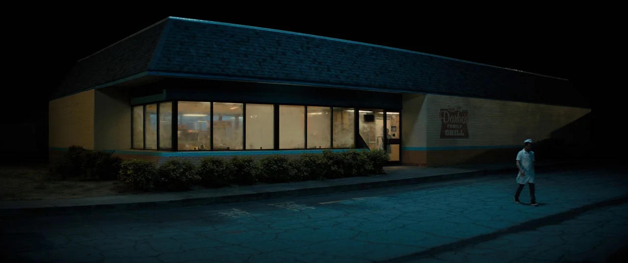 Brightburn (2019) movie still: wide — A lone restaurant building sits in a dark, empty parking lot at night. A lone man in a work uniform walks…